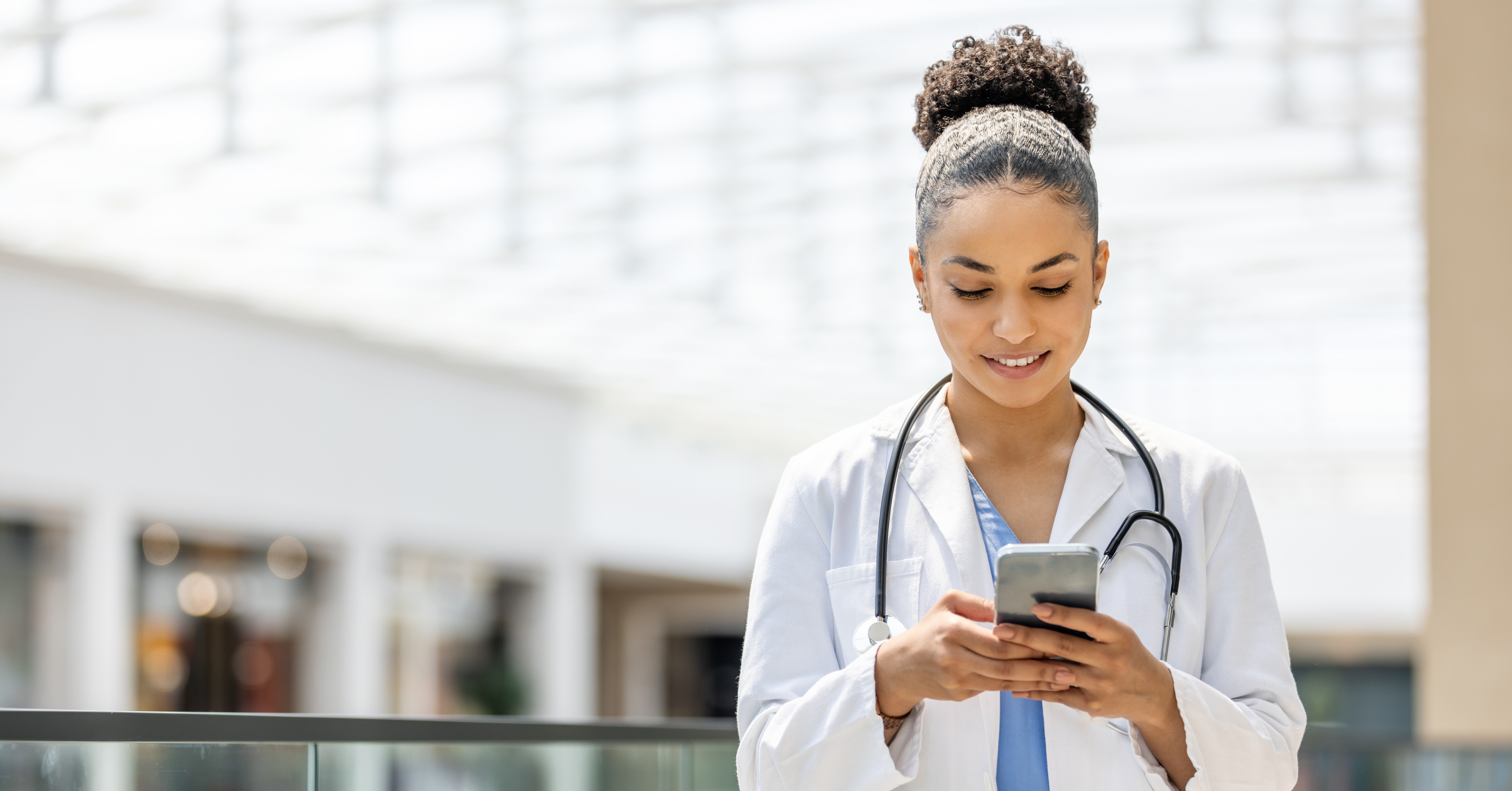Young physician looks down at her phone smiling 