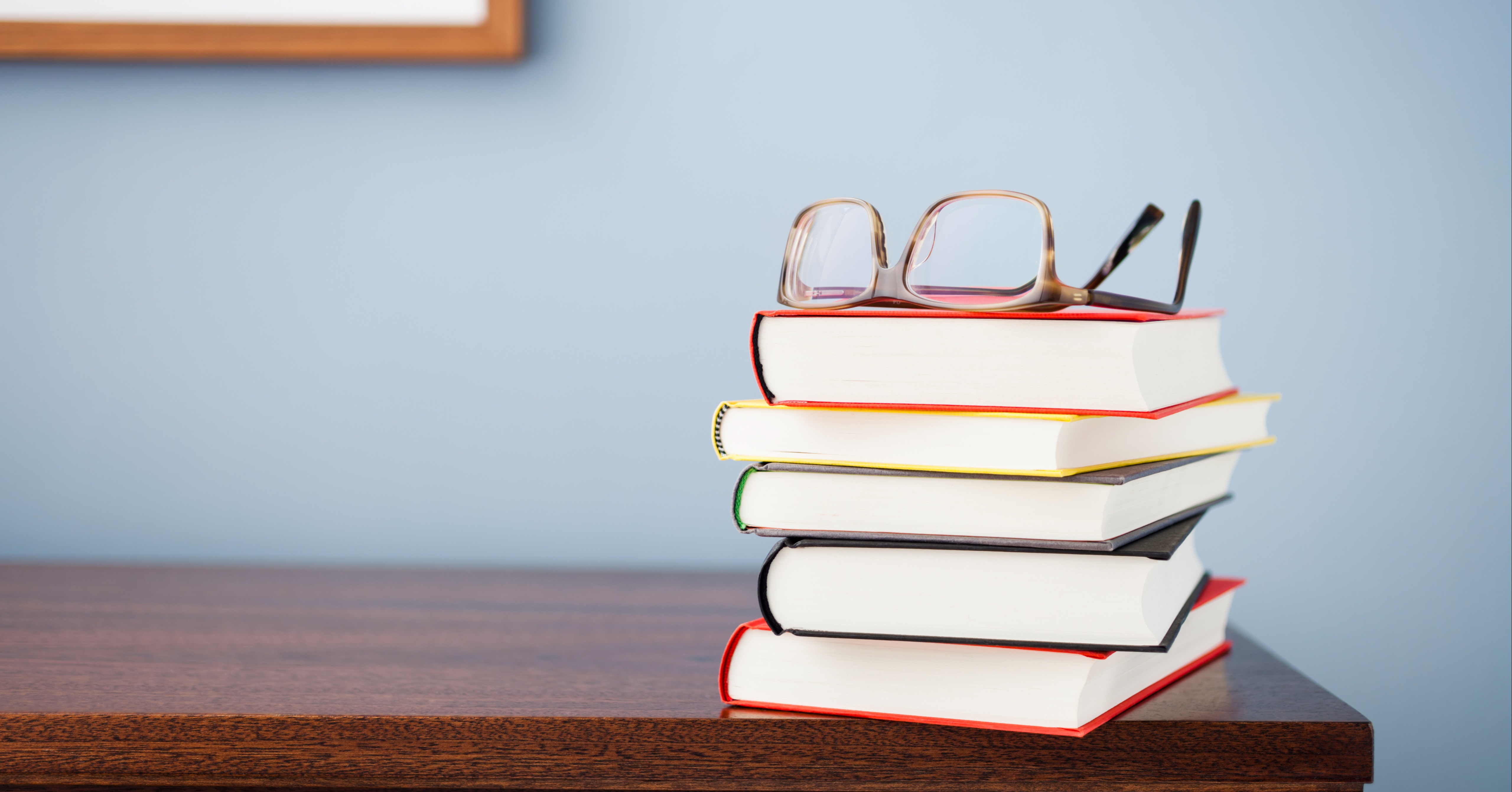 Stack of books on a desk with a pair of glasses on top